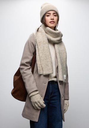 Cappotto in lana beige con grandi bottoni, abbinato a un berretto a costine e una sciarpa coordinati. Maglione grigio, jeans di denim e borsa a tracolla marrone. Guanti strutturati.