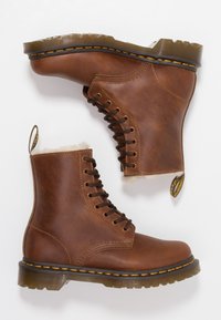 Botas de cuero marrón hasta el tobillo con un acabado texturizado, diseño con cordones, forro acolchado y suela de goma con un distintivo pespunte amarillo.