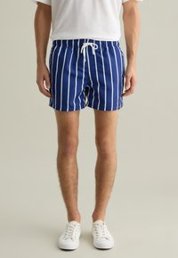 Pantaloni da bagno blu navy con strisce verticali bianche, vita elasticizzata, cordino regolabile e un piccolo emblema dorato sul lato.