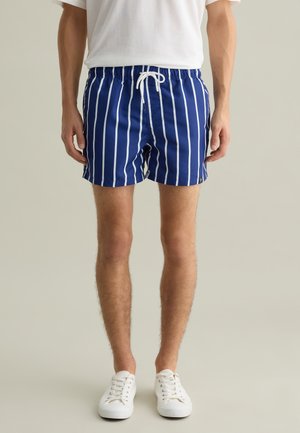 Pantaloni da bagno blu navy con strisce verticali bianche, vita elasticizzata, cordino regolabile e un piccolo emblema dorato sul lato.
