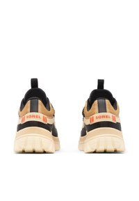 Musta- ja konjakinruskeat lenkkarit, joissa on teksturoitu päälliosa, oranssit brändäykset kantapäässä, paksut kermaan vivahtavat pohjat ja vetolenkki helppoa pukemista varten.