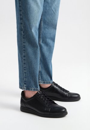 Czarne skórzane sneakersy o gładkim wykończeniu, z okrągłym noskiem i sznurowanym zapięciem, w połączeniu z jasnoniebieskimi, lekko skróconymi dżinsami.