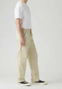 Lichtbeige elastische broeken met zijzakken, gecombineerd met een eenvoudig wit T-shirt en zwarte sneakers met witte zolen.