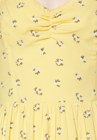 Robe jaune avec petit imprimé floral blanc, buste froncé et taille froncée.