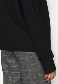 Svart stickad tröja med en avslappnad passform och långa ärmar, i kombination med grå rutiga byxor med ett rutmönster. Slät textur och avslappnad stil.