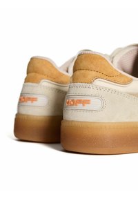 Zapatillas de color crema con detalles en gamuza marrón, suela de goma texturizada y marca "HOFF" en naranja en la parte trasera.
