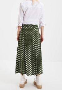 Jupe midi à pois verts avec un design fluide, fabriquée en tissu léger. Associée à des bottines blanches pour un contraste.