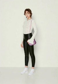 White textured long-sleeve top, black fitted pants, purple patterned handbag, and white sneakers, styled with relaxed wavy hair.