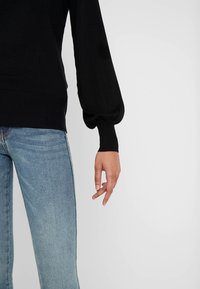 Czarny sweter z bufiastymi rękawami i żebrowymi mankietami, w połączeniu z jasnoniebieskimi dżinsami o prostym kroju. Tekstura wydaje się miękka i dziana.