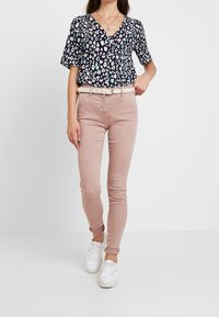 Blouse à manches courtes, couleur marine, avec un motif floral multicolore ; associée à un pantalon slim fit rose clair et des baskets blanches, avec une ceinture.