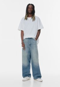 Prevelik sivo kratki rokav, in svetlo moder širok denim hlač. Ohlapen kroj, zbledela tekstura in minimalni šivi. Bele superge.