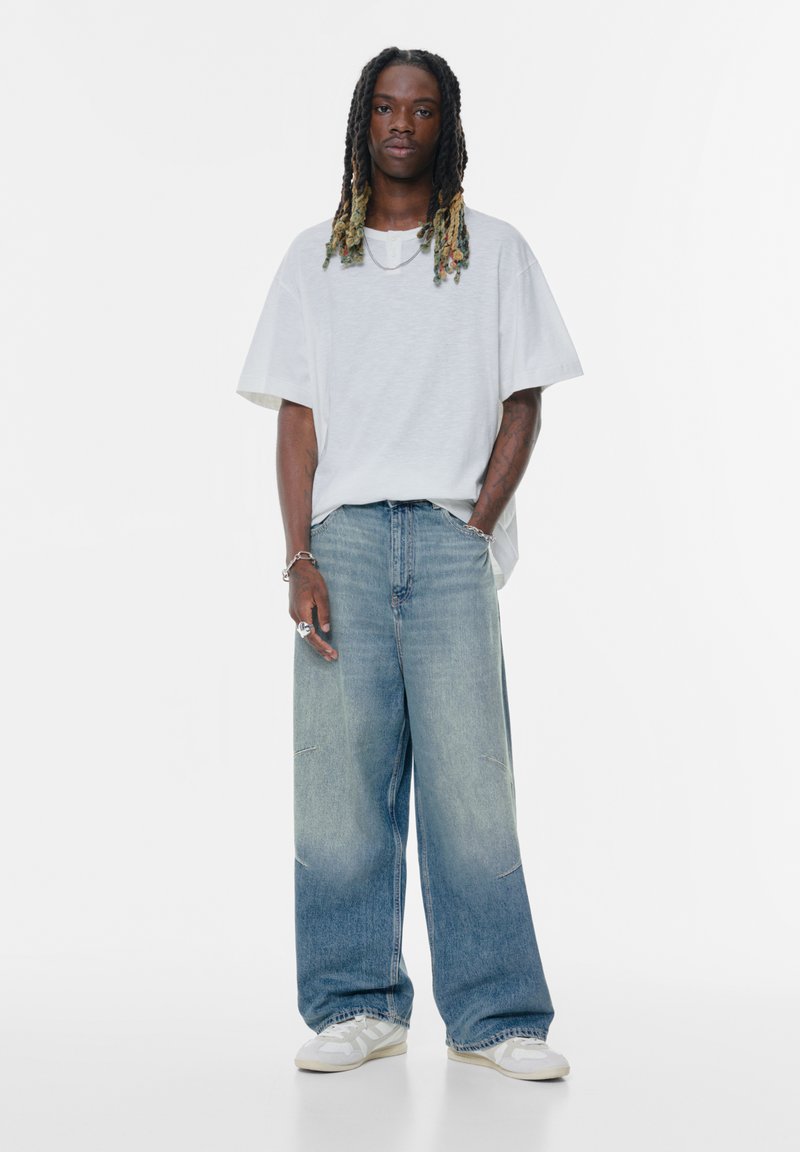 Prevelik sivo kratki rokav, in svetlo moder širok denim hlač. Ohlapen kroj, zbledela tekstura in minimalni šivi. Bele superge.