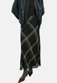 Falda larga negra con un patrón de cuadros en crema y óxido, hecha de un material fluido. Combinada con una chaqueta de cuero negra y tacones marrones.