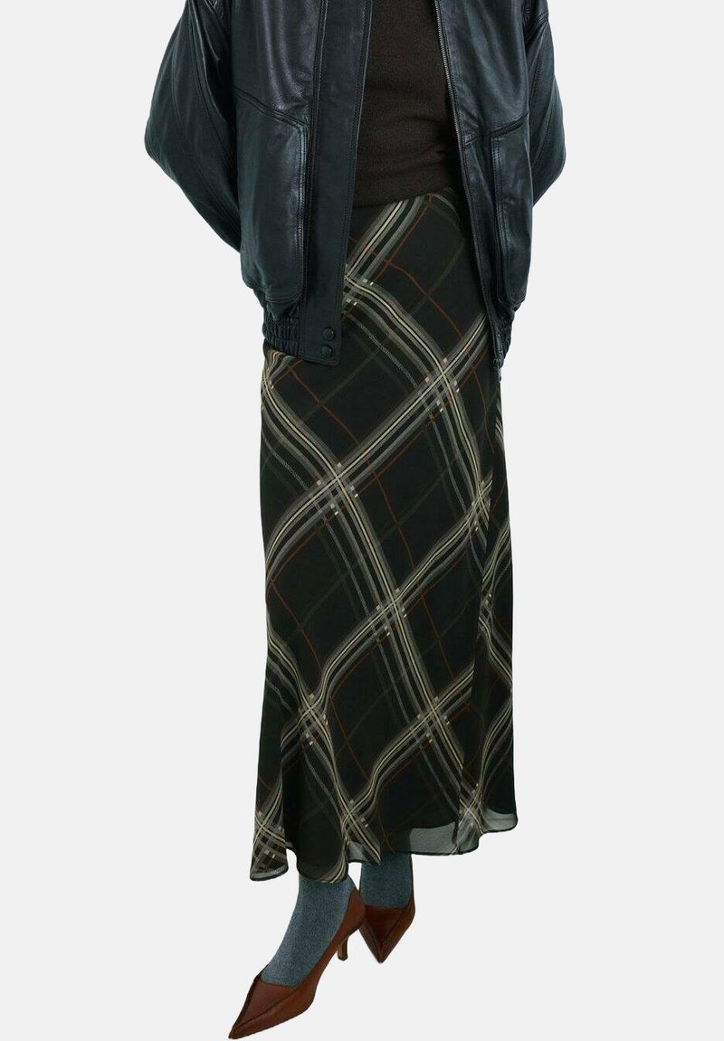 Falda larga negra con un patrón de cuadros en crema y óxido, hecha de un material fluido. Combinada con una chaqueta de cuero negra y tacones marrones.