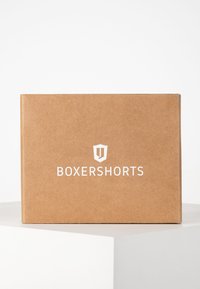 Brun pappeske med hvit tekst som leser "BOXERSHORTS" og et skjoldlogo foran. Glatt tekstur, rektangulær form.
