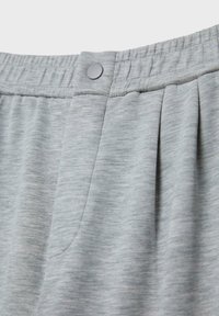 Gros plan sur un pantalon en tissu gris clair avec une ceinture élastique et un seul bouton-pression gris au centre.