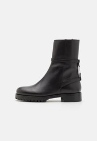 Černá kožená kotníková bota s kulatou špičkou, hladkým povrchem, bočním zipem a nízkou podrážkou s profilem, s minimalistickým designem.
