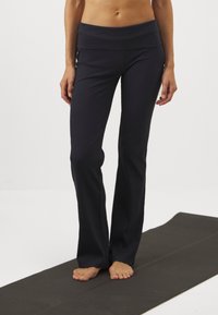 Sorte ribbede yogabukser med bred midje, slippende ben design og en glatt tekstur, parret med bare føtter på en yogamatte.