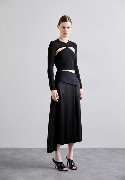 Black long-sleeve cut-out crop top paired with a high-low satin black skirt. Heeled black open-toe shoes complete the outfit.
