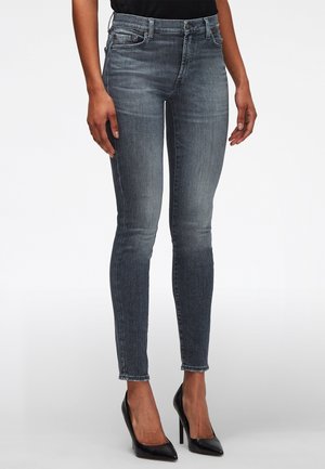 Jeans ajustados de color negro deslavado en una persona de pie que lleva tacones altos negros puntiagudos y una blusa negra.