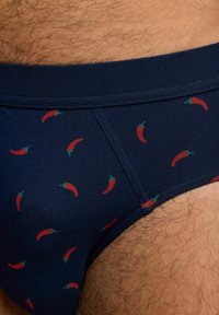 Bañador navy con un patrón de pimientos rojos y acentos verdes. Hecho de una tela suave con cintura elástica y acabado texturizado.