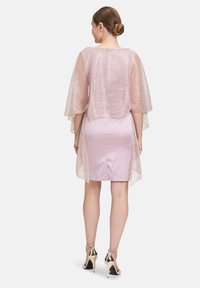 Roze satijnen jurk met een doorschijnende, gestructureerde overlay. Het ontwerp heeft brede mouwen en een lengte tot de knie, gecombineerd met metallic hakken.