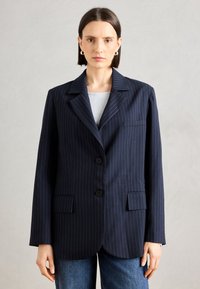 Námornícky pruhovaný blazer s klopami, dvomi gombíkmi a prednými vreckami; vyrobený z hladkej tkaniny, ponúkajúci voľný strih a dlhé rukávy.