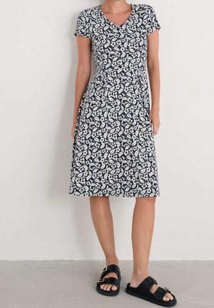 Navy floral dress with short sleeves, V-neck, and a cinched waist. Fabric features white leaf and flower patterns; paired with black sandals.