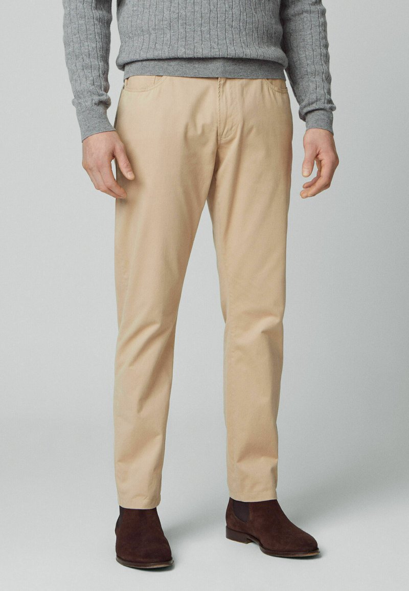 Beige bomulds-chinos med lige ben, der har sidelommer og en glat tekstur, parret med brune swede ankelstøvler.