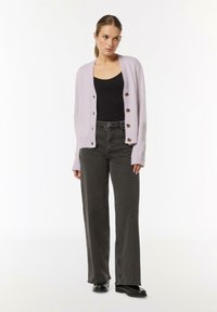 Hellblauer, gestrickter Cardigan mit gerippten Kanten und braunen Knöpfen. Kombiniert mit hochgeschnittenen, dunkelgrauen Jeans und schwarzen Stiefeln.