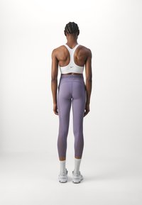 Biały stanik sportowy z plecami w stylu racerback, w zestawieniu z wysokim stanem lawendowych legginsów z efektem gradientu. Białe sneakersy i skarpetki.