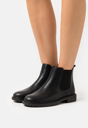 Svarta Chelsea-stövlar i läder med elastiska sidopaneler, rund tå och texturerad gummisula, designade för komfort och hållbarhet.