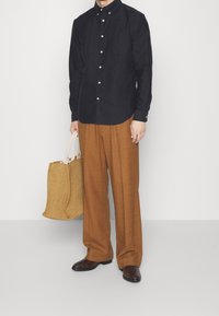 Camicia scura con colletto, pantaloni larghi marroni e borsa a tracolla intrecciata beige. Scarpe nere con motivo completano l'outfit.