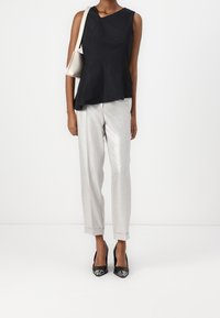 Top peplum senza maniche nero, pantaloni chiari in tessuto strutturato argentato e décolleté neri con accenti argentati. Piccola borsa a tracolla metallica.