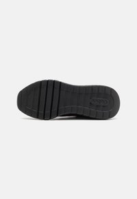 Black rubber shoe sole with textured grooves and a flat profile, featuring a prominent logo and segmented tread pattern for grip.