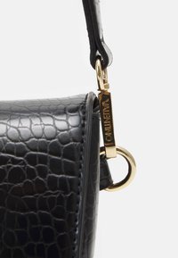 Borsa nera in ecopelle testurizzata con chiusura e anello in metallo dorato. Presenta una forma strutturata e dettagli di cucitura visibili.