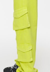 Jasně limetkově zelené cargo kalhoty vyrobené z bavlny, s několika bočními kapsami a rovnými nohavicemi. Doplňují je černé boty.
