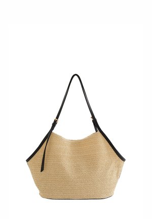 Sac cabas en paille tissée beige avec bandoulière noire réglable et garniture, ouverture en haut et forme décontractée et ample.