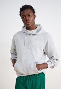 Hallide hallitus, millel on kapuuts, kaks esikot ja paelad; sisaldab väikest valget logo. Kombineeritud tekstureeritud roheliste lühike pükstega.