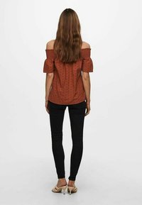 Rustfarvet off-the-shoulder bluse med puffærmer, struktureret stof, parret med sorte skinny jeans og beige hælede sandaler.