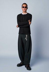 Čierne rebrované tričko s dlhým rukávom s bielym golierom, voľné čierne nohavice a robustné čierne topánky; doplnené o kľúčenky.