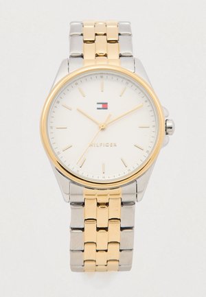 Zilveren en goudkleurige polshorloge met een witte wijzerplaat, gouden wijzers en uurmarkeringen. Bevat een gepolijste metalen armband met schakels. Tommy Hilfiger-logo zichtbaar.