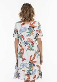 Bloemjurk gemaakt van lichte stof, met een witte achtergrond en kleurrijke bladeren en bloemenpatronen, korte, gerimpelde mouwen en een gestrikte taille.