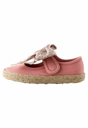 Pink canvas shoe with a floral fabric bow, espadrille-style jute sole, round toe, and side Velcro strap. Smooth texture with stitching detail.