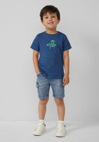 Marineblauwe katoenen T-shirt met groene dinosaurustekening, gecombineerd met denim shorts en witte sneakers. Eenvoudig ontwerp en casual pasvorm.