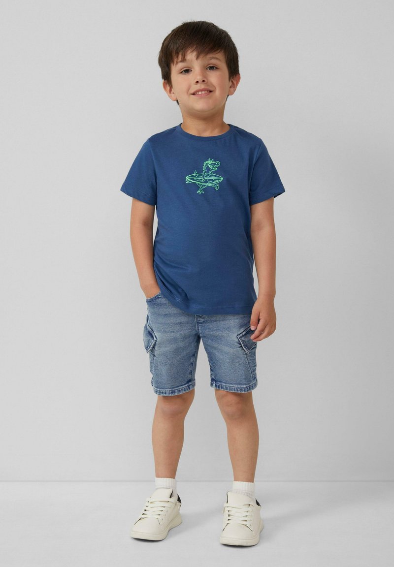 Marineblauwe katoenen T-shirt met groene dinosaurustekening, gecombineerd met denim shorts en witte sneakers. Eenvoudig ontwerp en casual pasvorm.