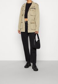 Beige užitková bunda s několika kapsami, kombinovaná s černým crop topem a černými jeansy s vysokým pasem. Černé kotníkové boty a černá kabelka.