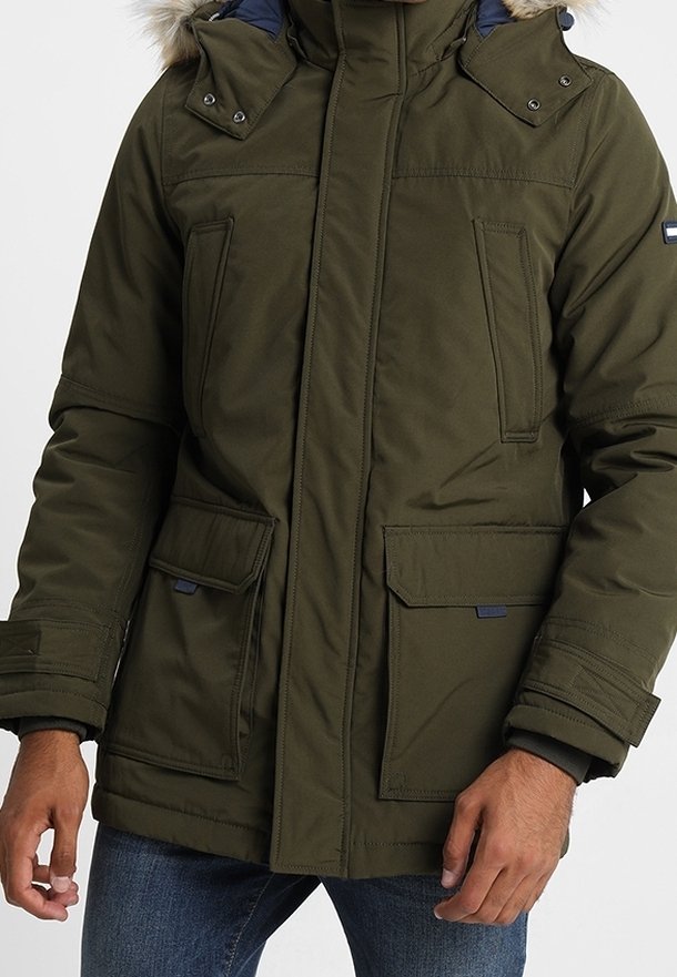 Olivgrön parkasjacka med huva i fuskpäls, tryckknappdetaljer, två frontfickor och dragkedjestängning. Texturerad tyg med ett lager på lager-design.