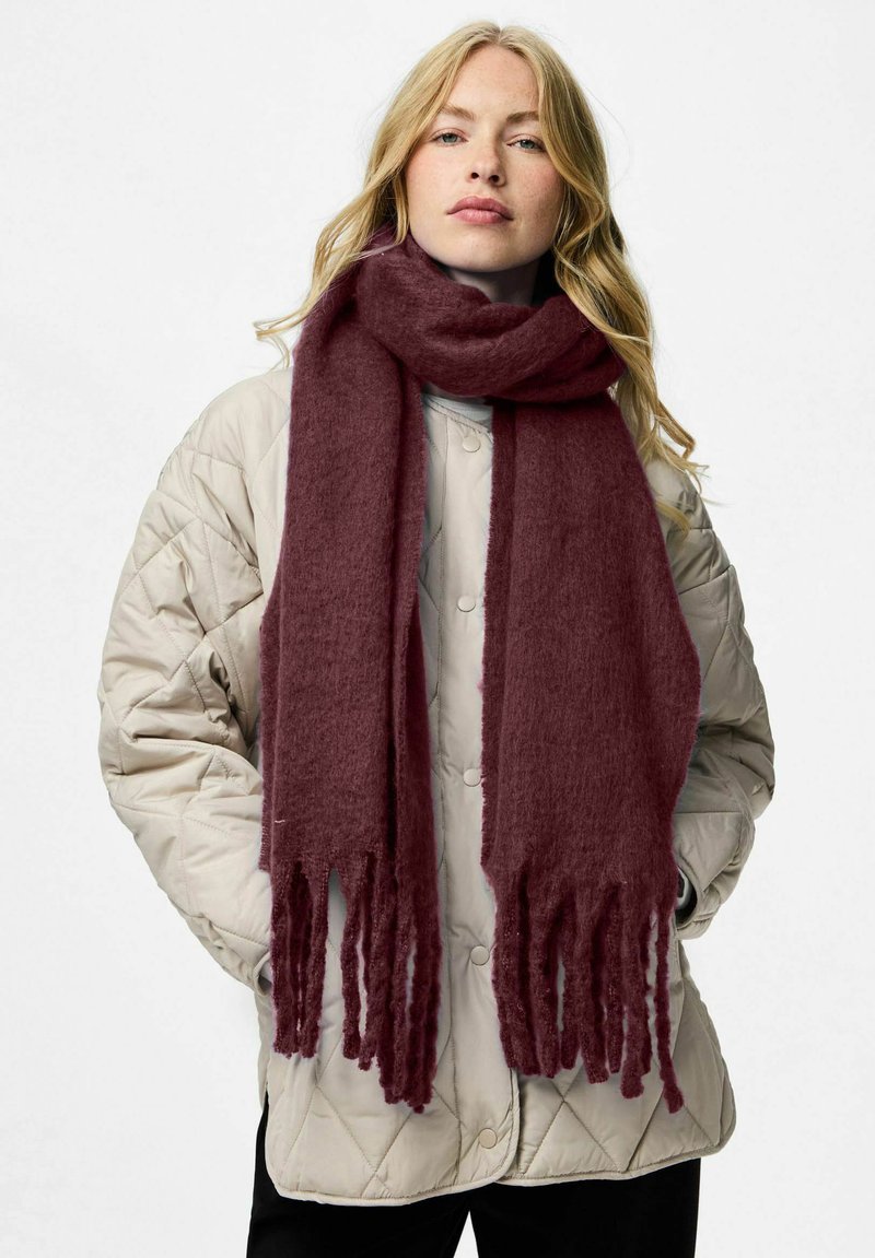 Burgundy tørklæde lavet af blødt, tekstureret stof med frynser, båret over en let quiltet jakke, hvilket skaber et hyggeligt lag-på-lag look.