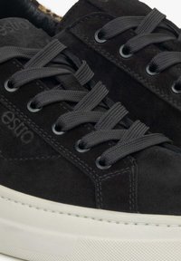 Black suede sneakers with gray laces and eyelets. Notable white rubber sole with textured detailing. Logo embossed on the side.